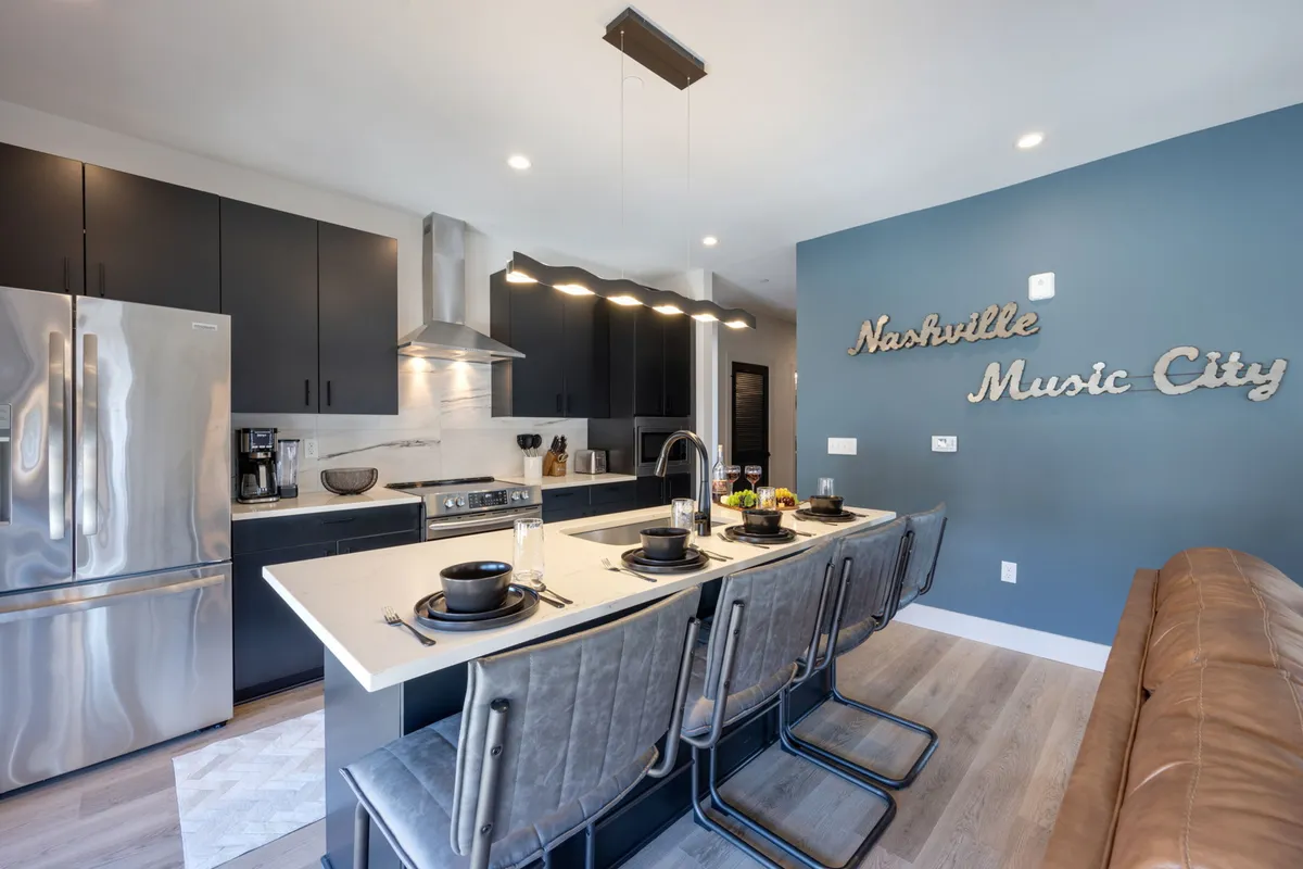 A warm, inviting kitchen featuring a spacious island, modern stainless steel appliances, and distinctive Nashville Music City wall art. The open layout allows for easy entertaining and group cooking, with city-themed decor adding a local flair.