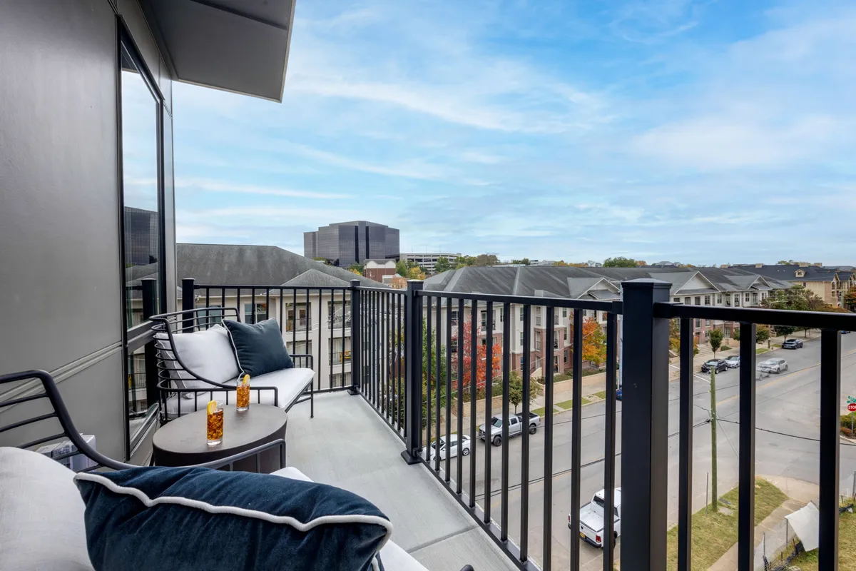 A serene balcony scene overlooking the city, featuring inviting seating and a decorative drink. The city skyline glows in the background, creating an ideal setting for relaxing or socializing after a night out.