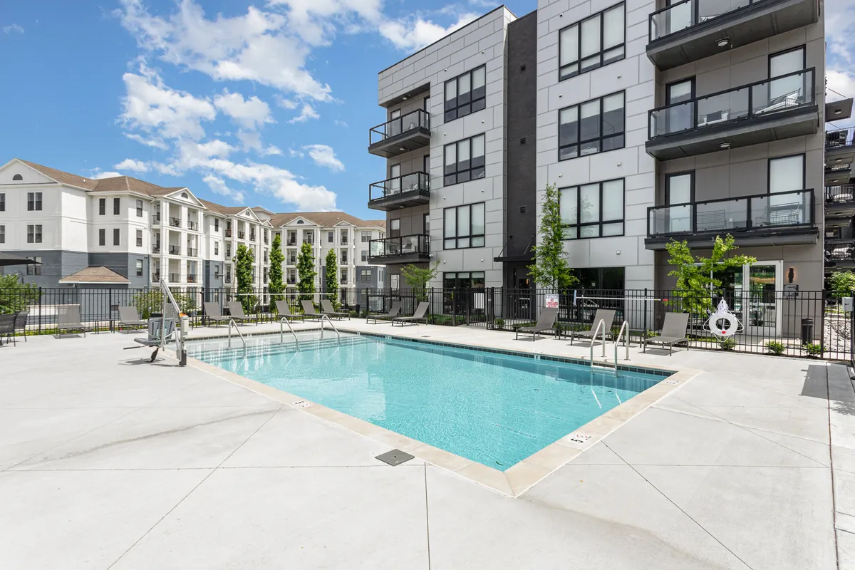 A sparkling swimming pool takes center stage, surrounded by sun loungers and flanked by modern balconies and lush landscaping. The setting evokes a sense of relaxation and community, ideal for both group celebrations and quiet afternoons under the sun.