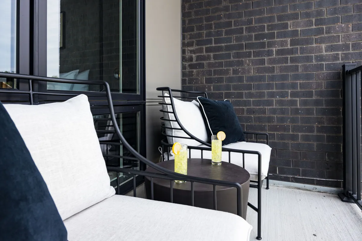 An inviting exterior scene with metal chairs and a round table topped with drinks featuring lemon garnish, against a brick wall backdrop. The setting is relaxed, perfect for enjoying coffee or cocktails outdoors, with a hint of urban charm.