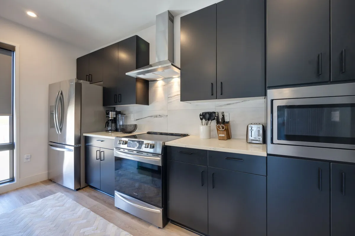 A sleek kitchen featuring stainless steel appliances, black cabinetry, a white marble backsplash, and a chevron-patterned floor. The space exudes modernity and functionality, ideal for both gourmet cooking and casual dining.
