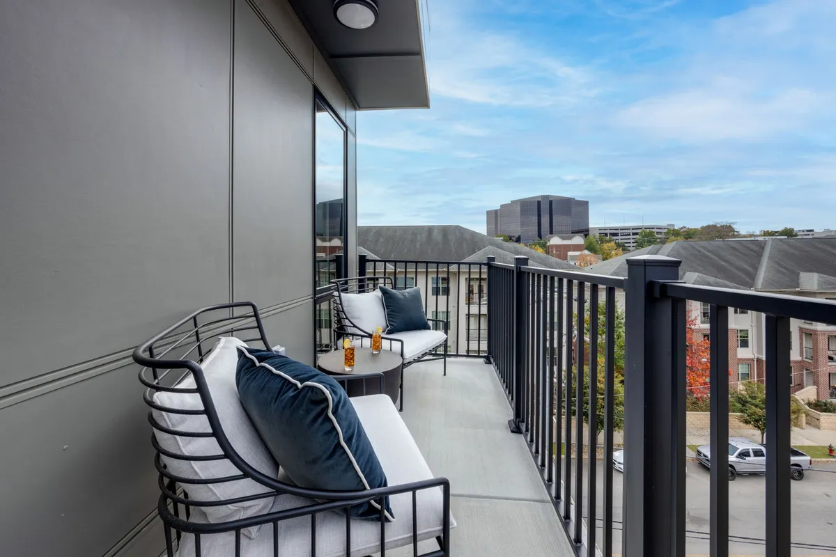 An inviting balcony with cozy seating, decorative pillows, a table set with drinks, and a stunning cityscape view. The outdoor space is styled for comfort and relaxation, offering an urban vantage point to enjoy fresh air and sunsets.